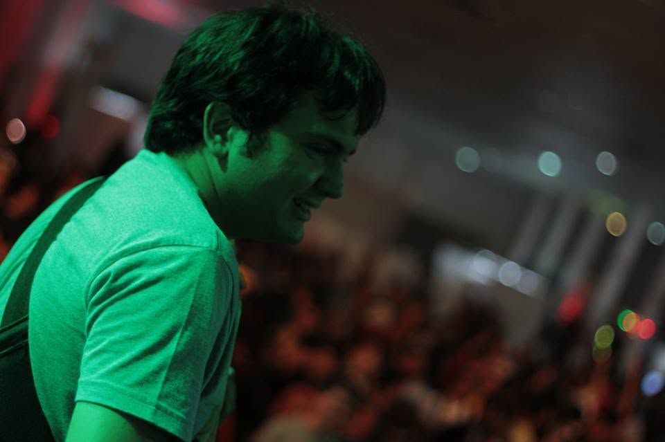 Diego Volpatto sorrindo durante uma apresentação, com o público ao fundo.
